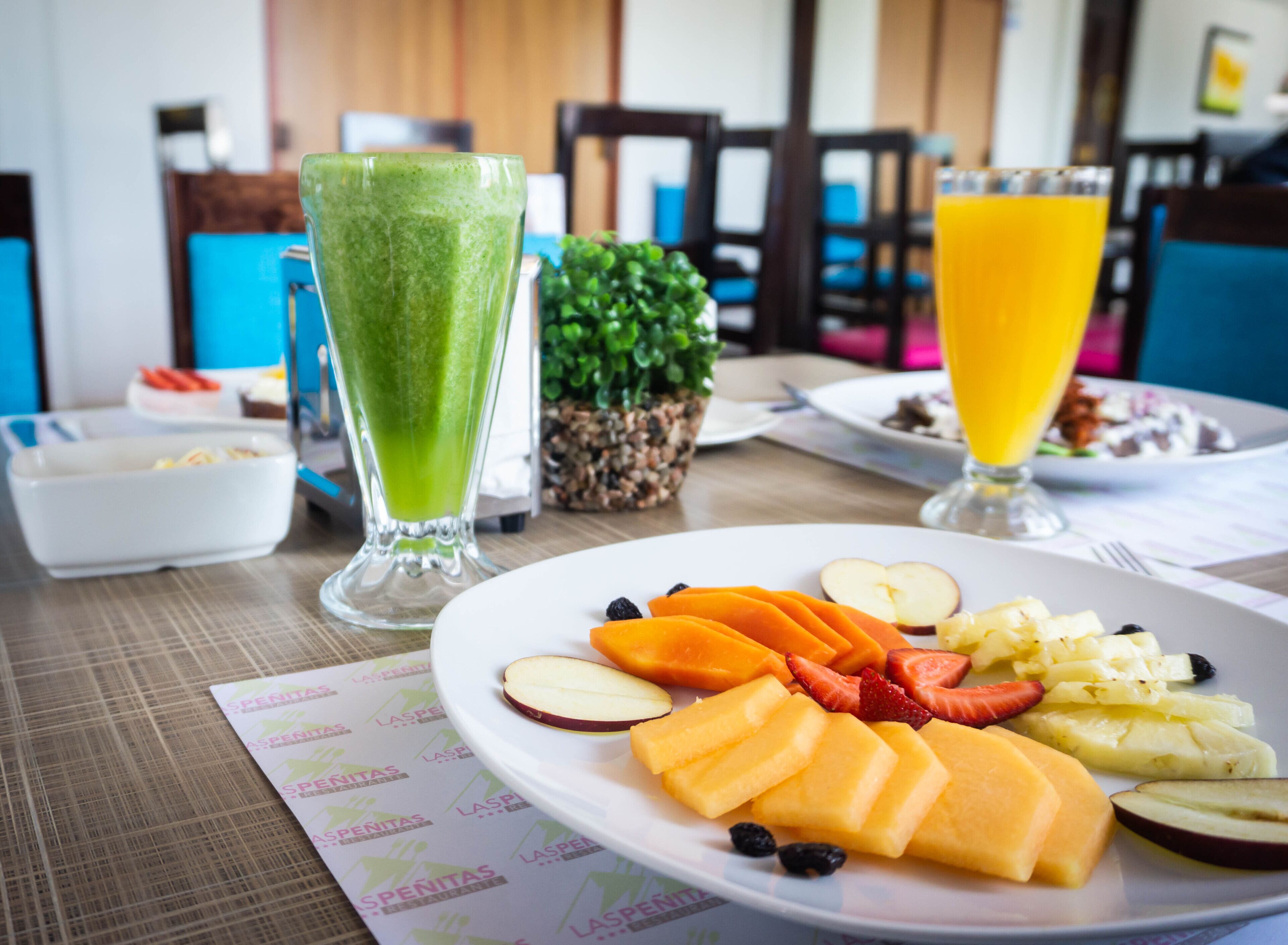 A breakfast setting with a plate of fruit, a green smoothie, and a glass of orange juice on a table.