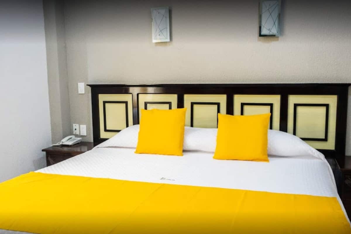A hotel room with a large bed, two pillows, a nightstand, and a wall-mounted light fixture.