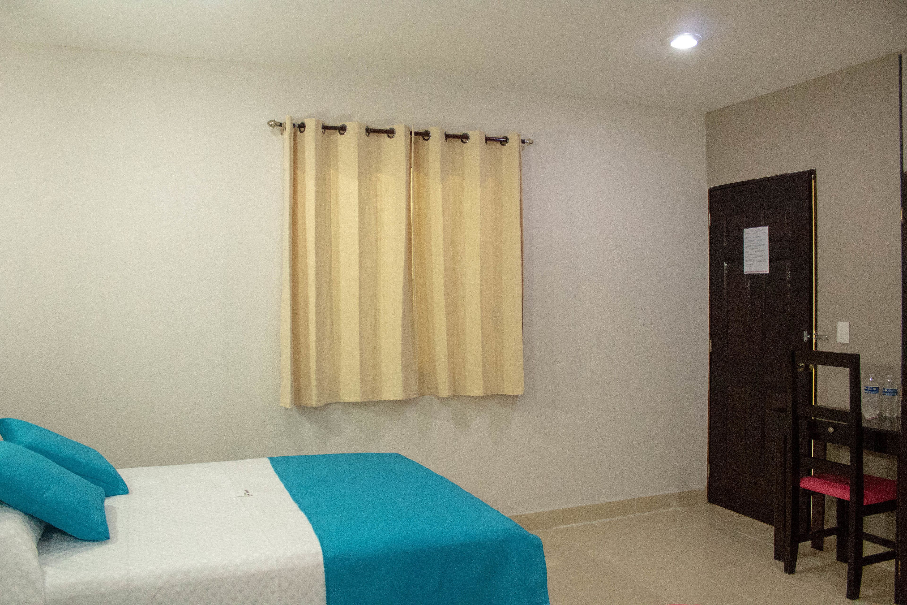 A hotel room with a bed, a chair, a curtain, and a door.