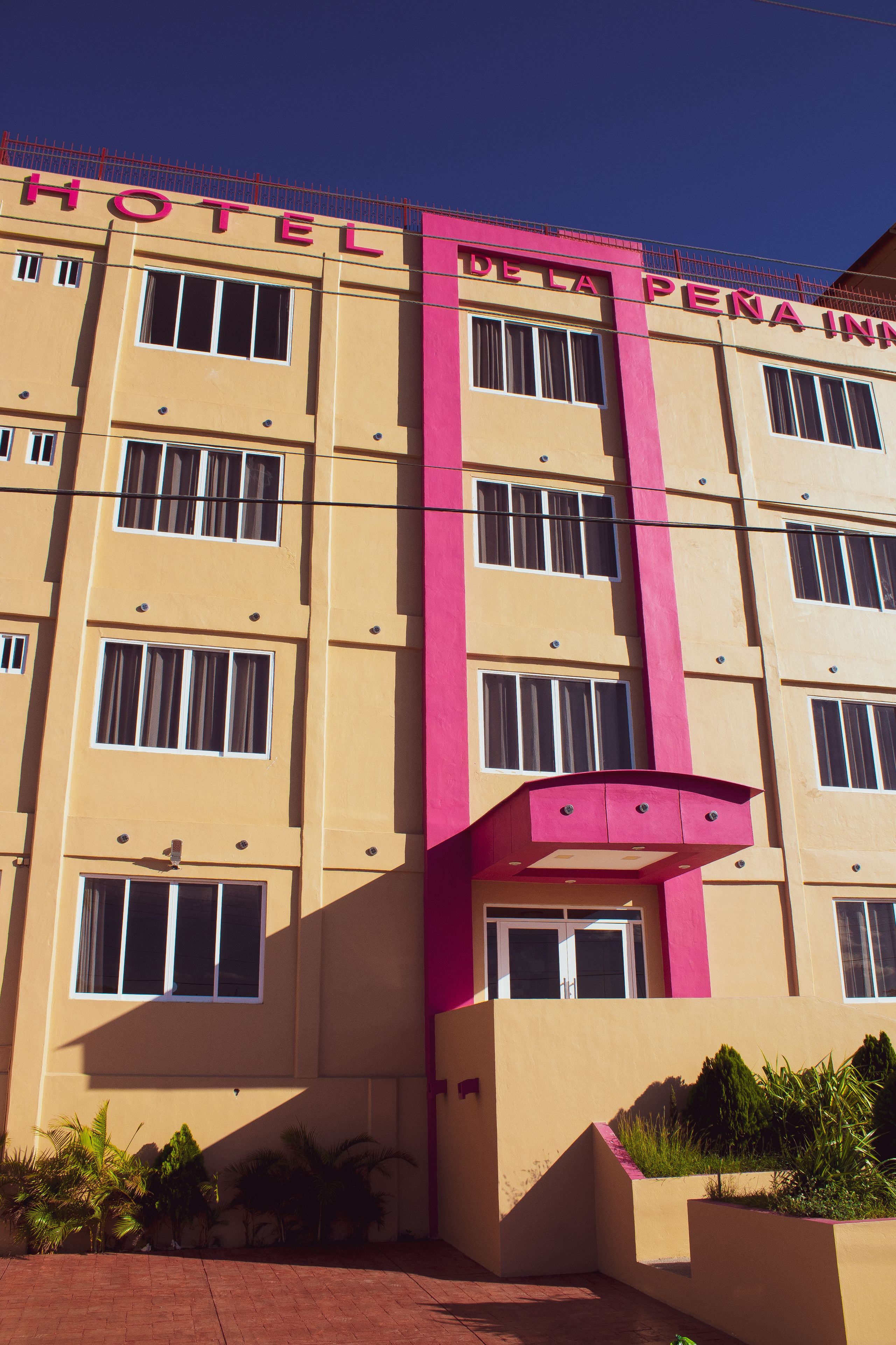 A hotel building with multiple floors, large windows, and a prominent pink and beige color scheme.