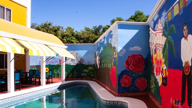 Un espace piscine agrémenté d’une fresque murale, d’un auvent jaune et offrant une vue sur un bâtiment.