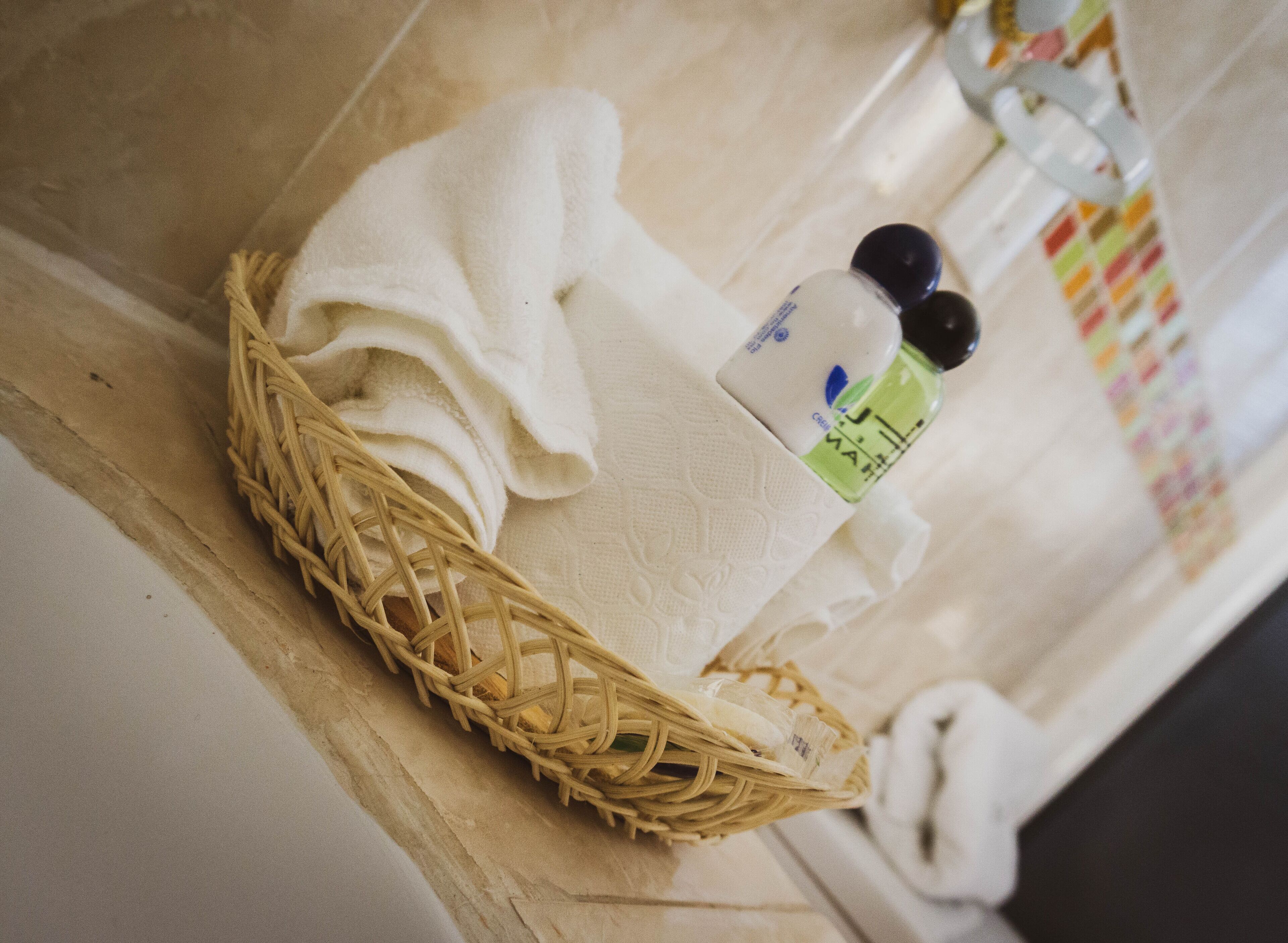 A bathroom with a wicker basket containing a white towel and a bottle of liquid soap.