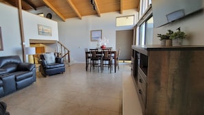 A spacious living area with a black leather sofa, a dining table with chairs, and a staircase leading to an upper level.