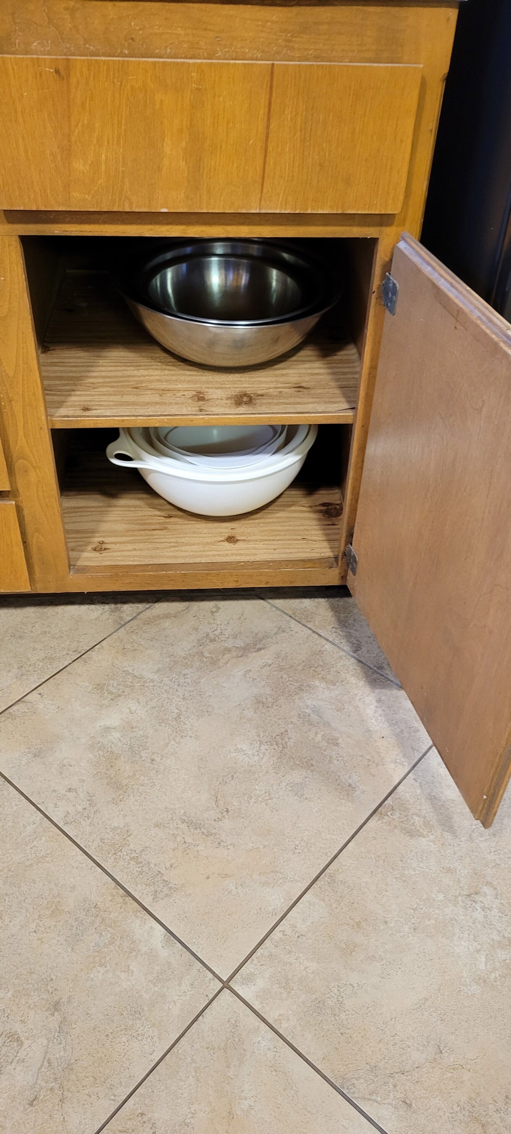 A wooden cabinet with two shelves, one containing a stainless steel bowl and the other a white bowl.