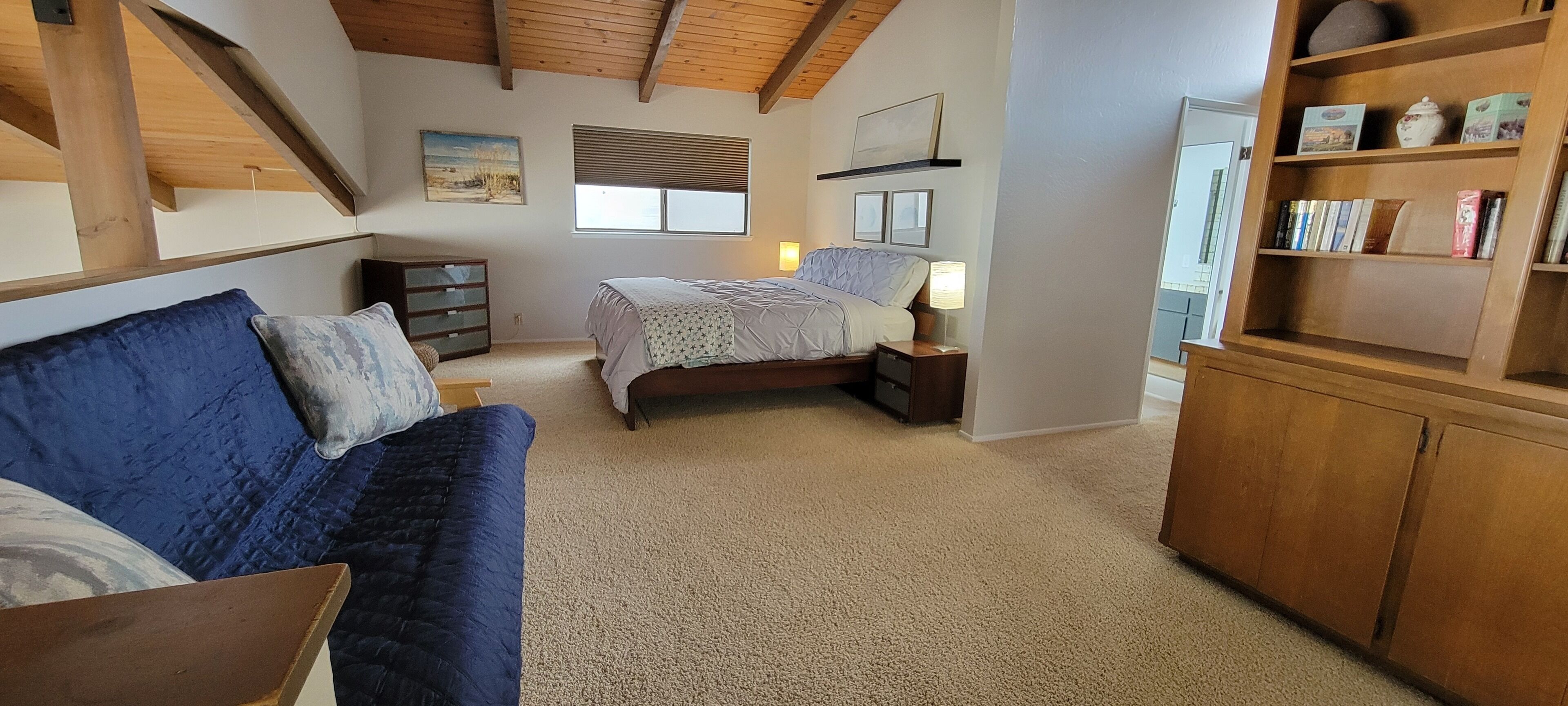 A bedroom with a bed, a blue sofa, a wooden cabinet, and a window.