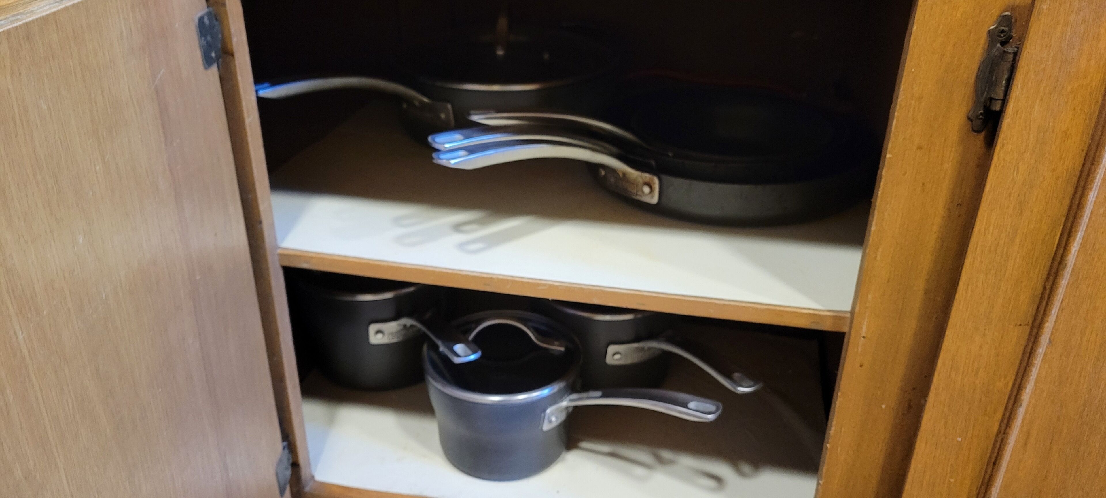 Un meuble de cuisine contenant des ustensiles de cuisine, notamment une poêle, des casseroles et une bouilloire.