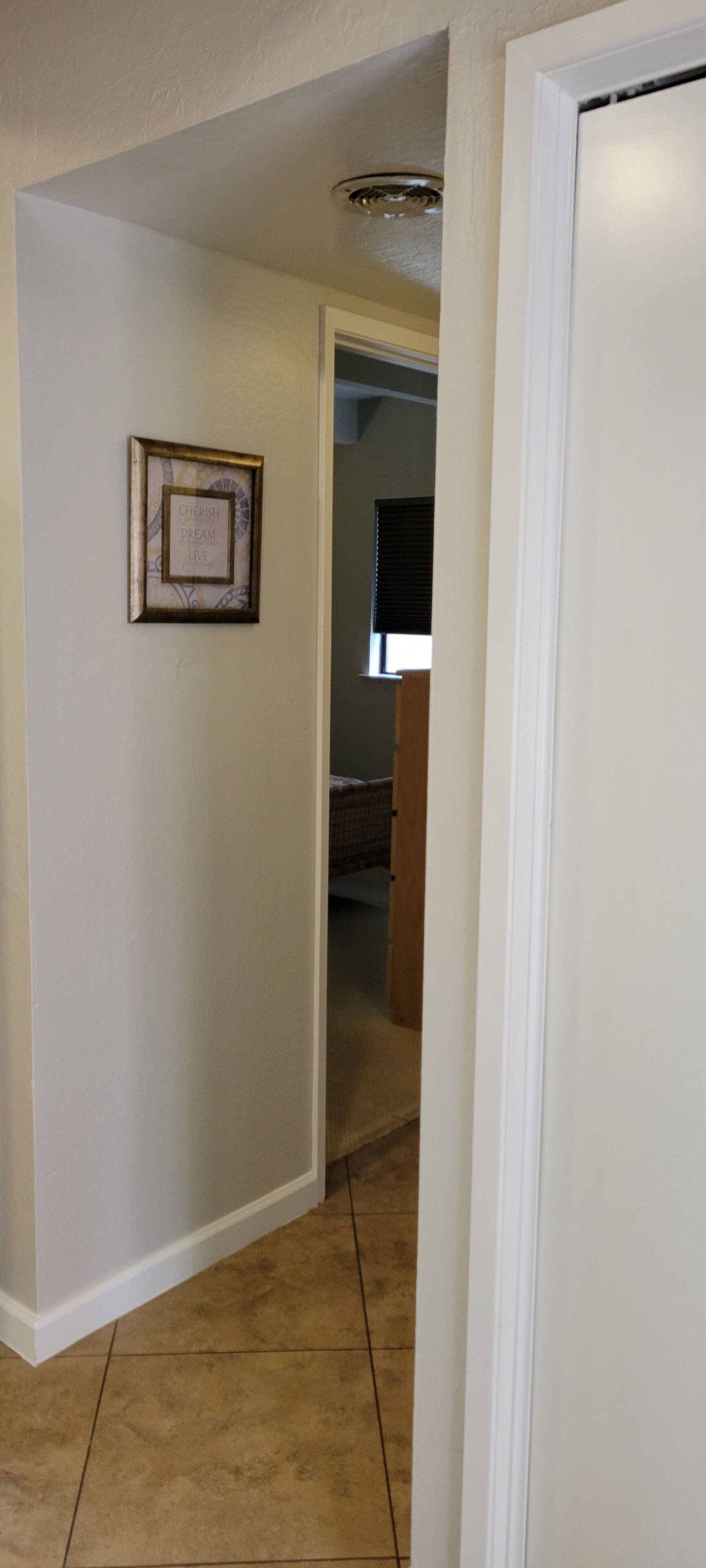 A hallway with a framed inspirational quote on the wall, a door on the right, and a staircase leading to another room.