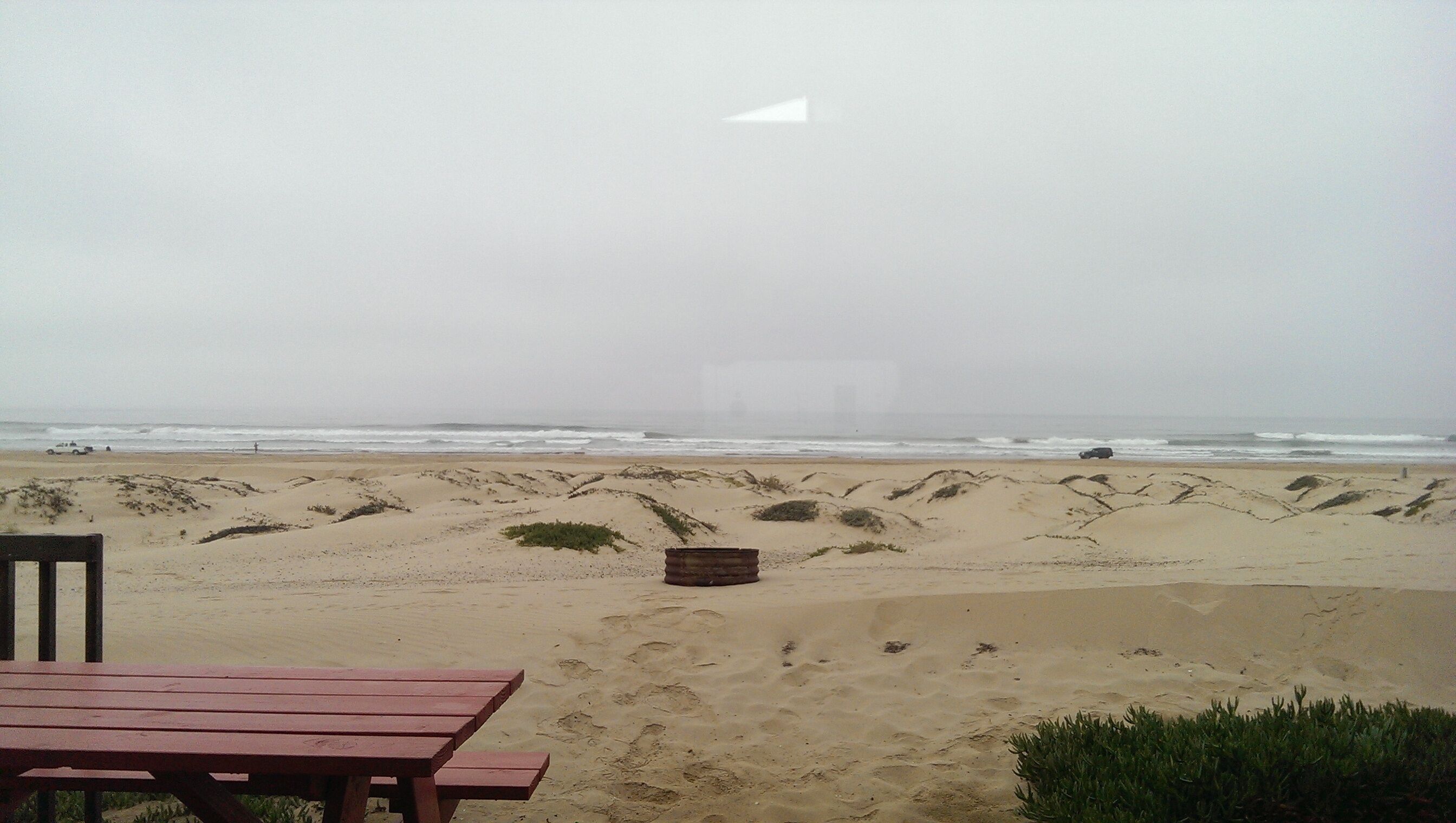 A beach with a wooden bench and a trash bin.
