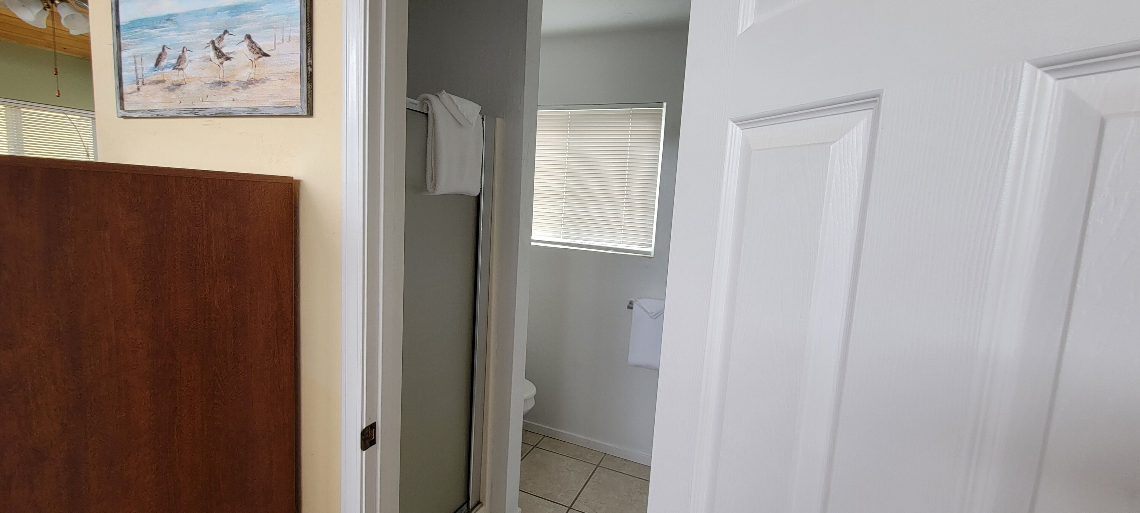 Une salle de bain avec douche, toilettes et une fenêtre équipée de stores.