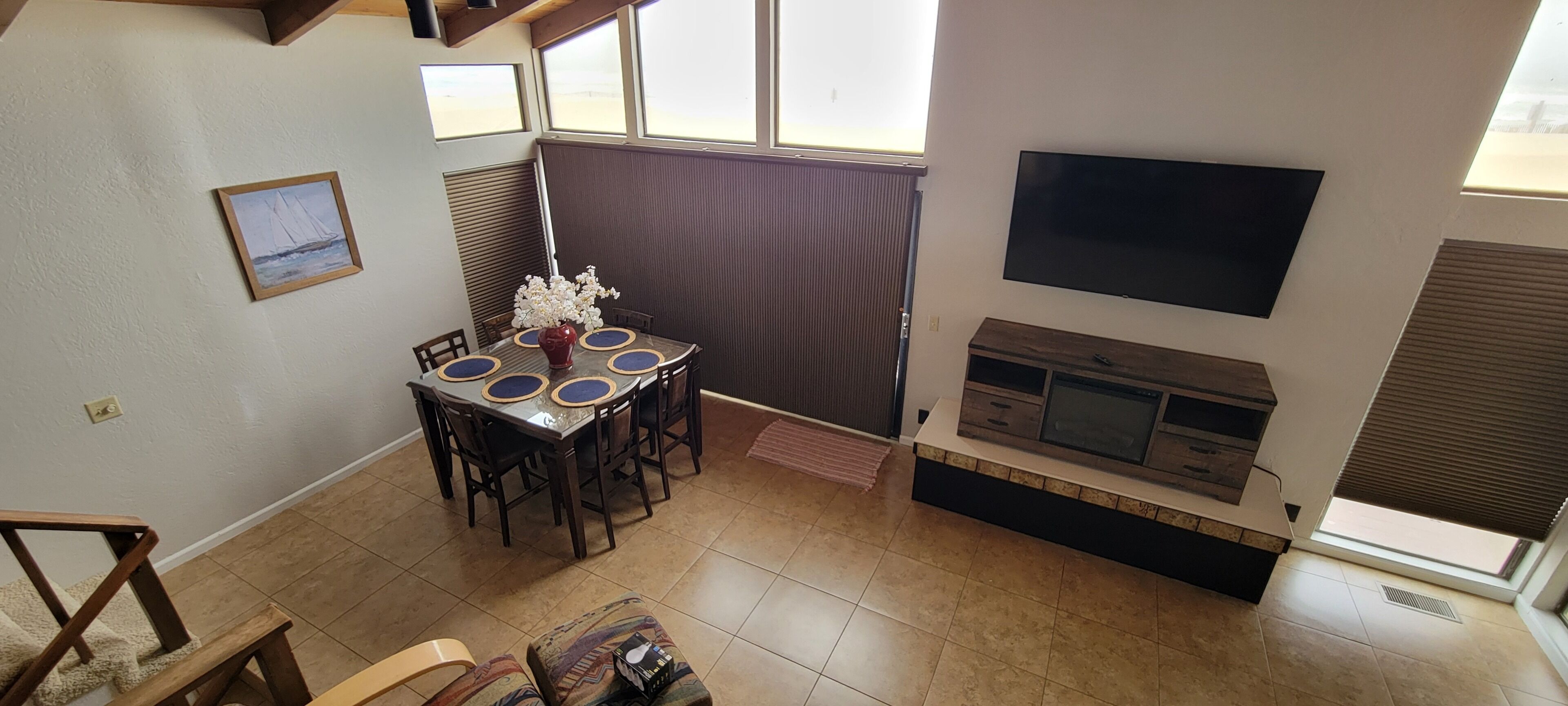 A dining area with a table and chairs, a fireplace, a TV mounted on the wall, and a window with blinds.