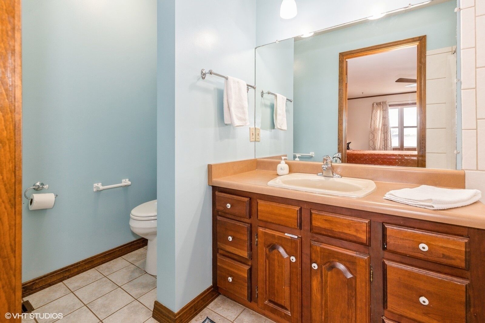 Un baño con tocador de madera, lavabo y espejo.