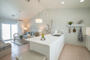 A modern kitchen with a central island, white cabinetry, and a dining area with wicker furniture.