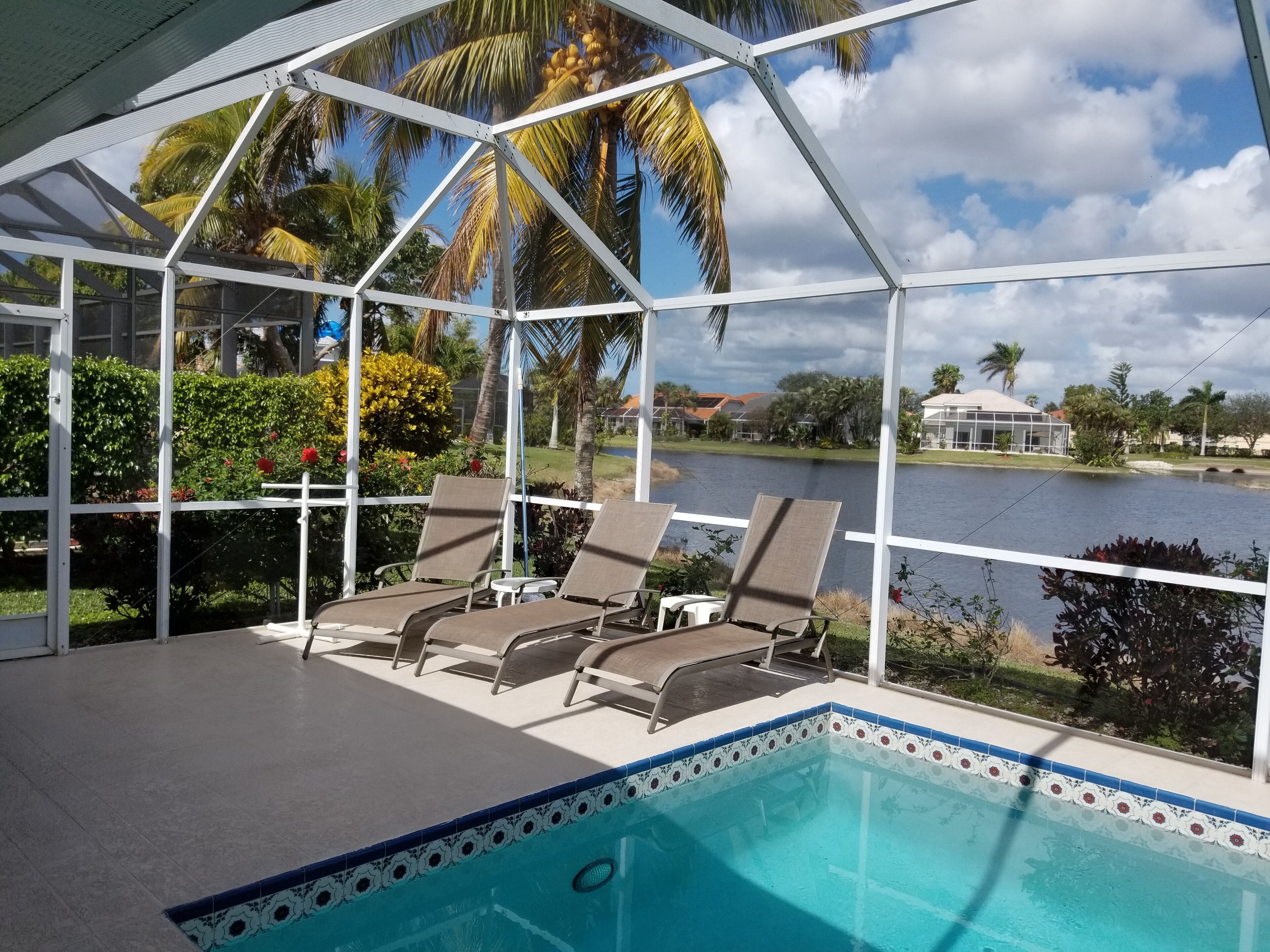 Un área de piscina techada con sillones de descanso, vista despejada de un lago y palmeras al fondo.