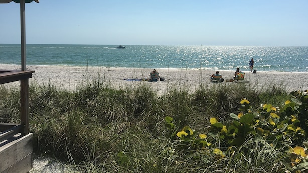A beach with people relaxing on the sand, a boat in the water, and a wooden structure in the foreground. - Crown Pointe Home with Lake Views! (Naples)