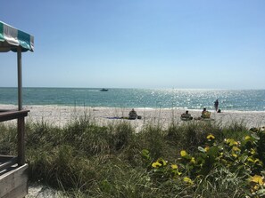 A beach with people relaxing on the sand, a boat in the water, and a wooden structure in the foreground. - Crown Pointe Home with Lake Views! (Naples)