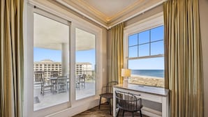 A room with a large window overlooking a beach, a desk with a chair, and a view of a building across the balcony. - Ocean Place Resort~incredible views and oversized balcony (Fernandina Beach)