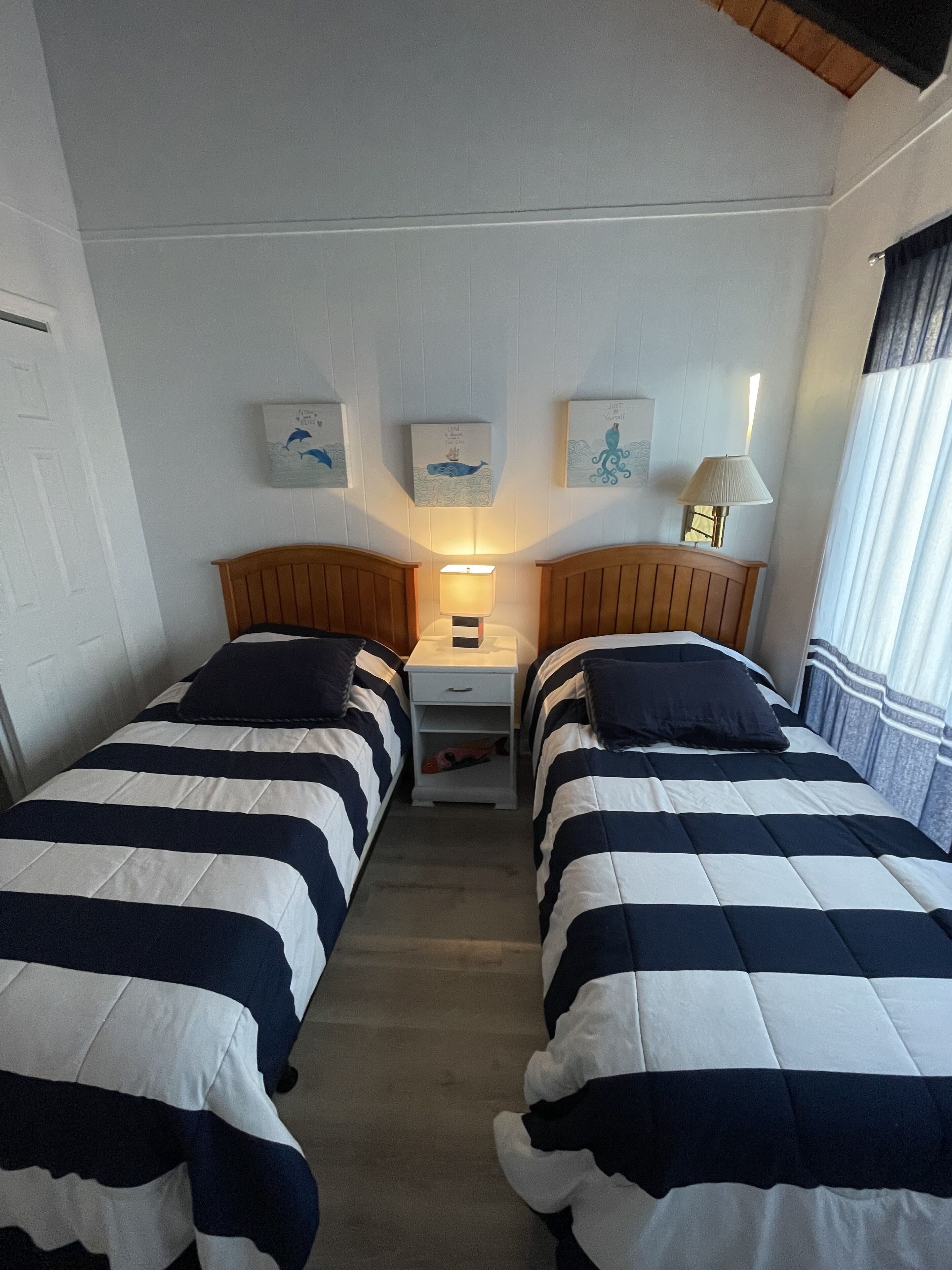 A hotel room with two single beds, a nightstand with a lamp, and wall art depicting marine life.