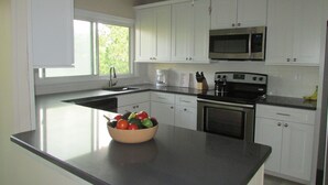A modern kitchen with white cabinets, a black countertop, a stove, a microwave, and a bowl of fruit on the island. - Oceanblock,  steps to best beach in Bethany (Bethany Beach)
