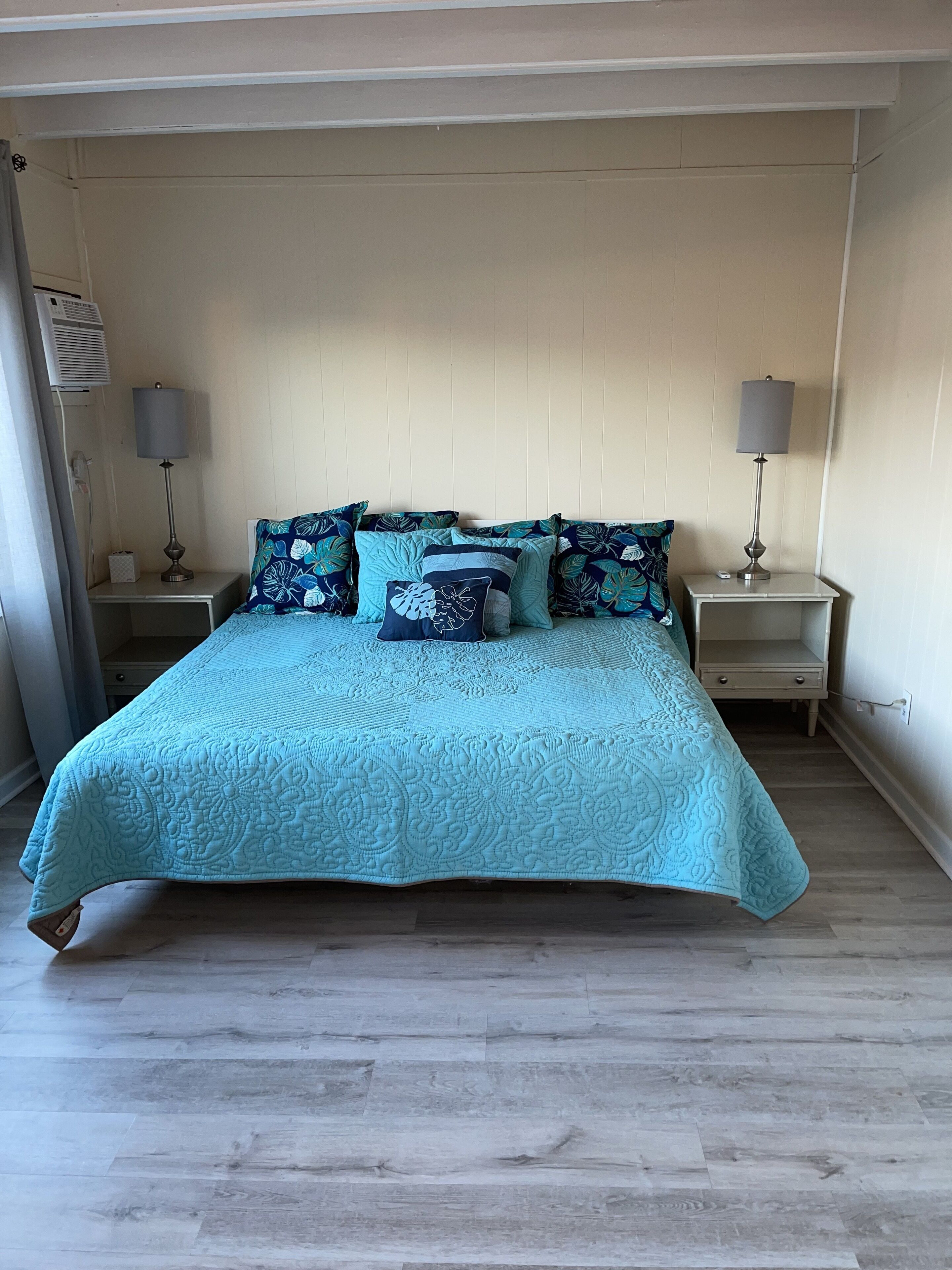 Ein Bett mit einer hellblauen Steude, zwei Nachttische mit Lampen und ein Holzboden.