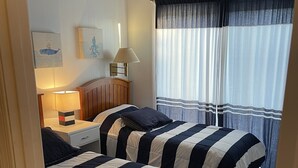 A room with two beds, a nightstand, a lamp, and a window with curtains. - Oceanblock,  steps to best beach in Bethany (Bethany Beach)