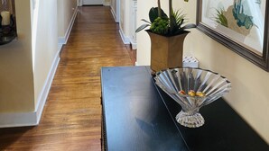 Un corridoio con pavimento in legno, un tavolino consolle nero con una ciotola di vetro decorativa, un'orchidea in vaso e una stampa botanica incorniciata appesa alla parete.