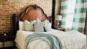 Una camera da letto con parete in mattoni, struttura letto in legno, ventilatore a soffitto e finestra con tende.