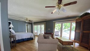 A spacious room with a bed, a sofa, a dining table, and a ceiling fan.
