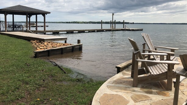 A lakeside deck with Adirondack chairs, a wooden dock, and a gazebo.