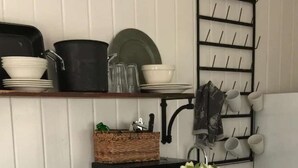A kitchen with a white stove, a microwave, and a sink. There are shelves with dishes and a rack with cups and utensils. - Romantic Refreshing 1890s Cottage Uptown Eureka Springs (Eureka Springs)
