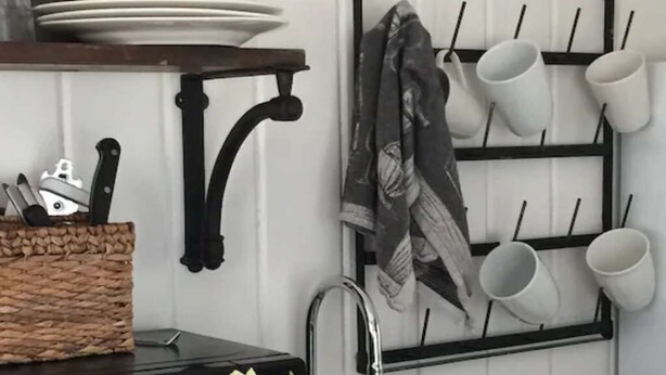 A kitchen with a black microwave, a sink, and a hanging rack with cups and a towel. - Romantic Refreshing 1890s Cottage Uptown Eureka Springs (Eureka Springs)