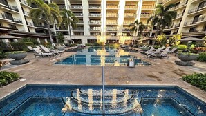 Ein Hotelpoolbereich mit einer zentralen Fontäne, Liegestühlen und einem mehrstöckigen Gebäude im Hintergrund.