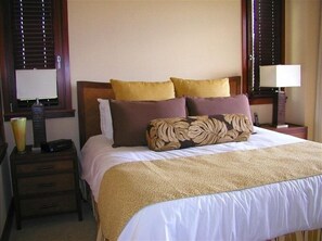 Una habitación de hotel con cama, una mesita de noche con lámpara y una ventana con persianas.