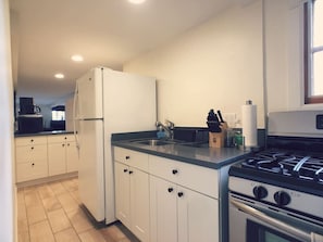 Una cocina moderna con armarios blancos, encimera negra, estufa a gas y refrigerador.