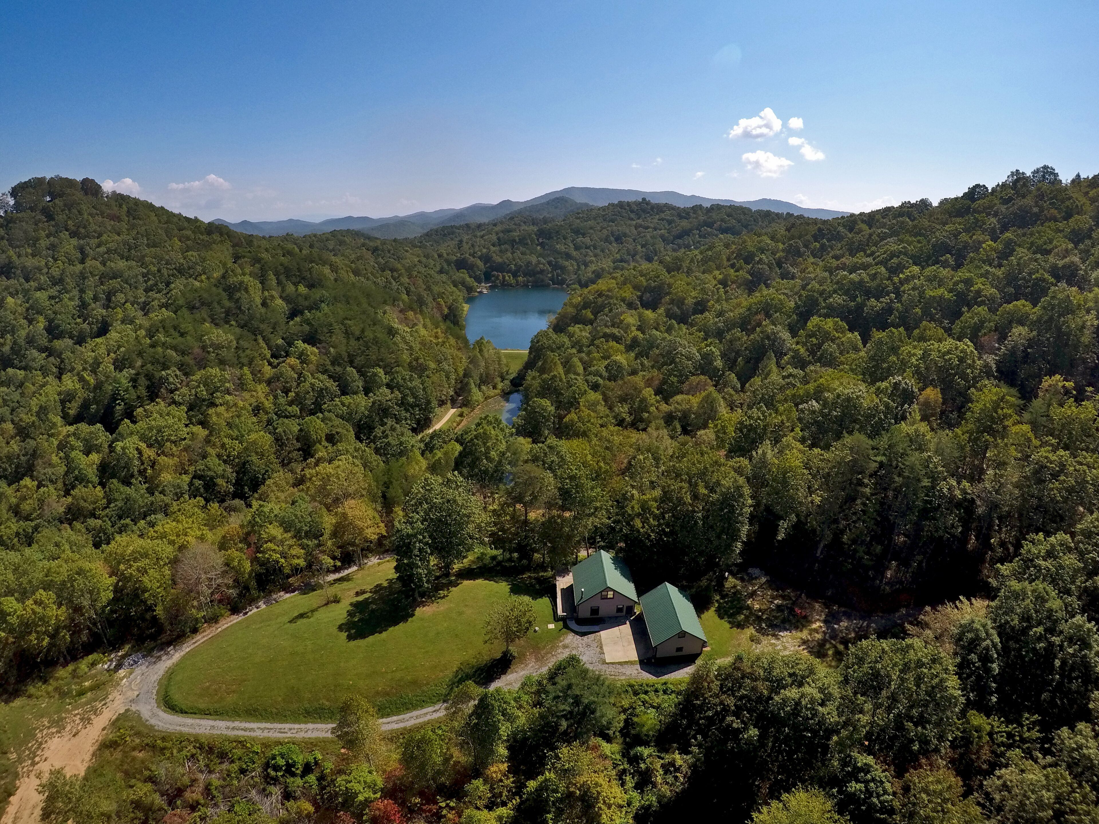 Une maison dotée d’un toit végétalisé, nichée dans une vallée boisée, avec un lac en arrière-plan.