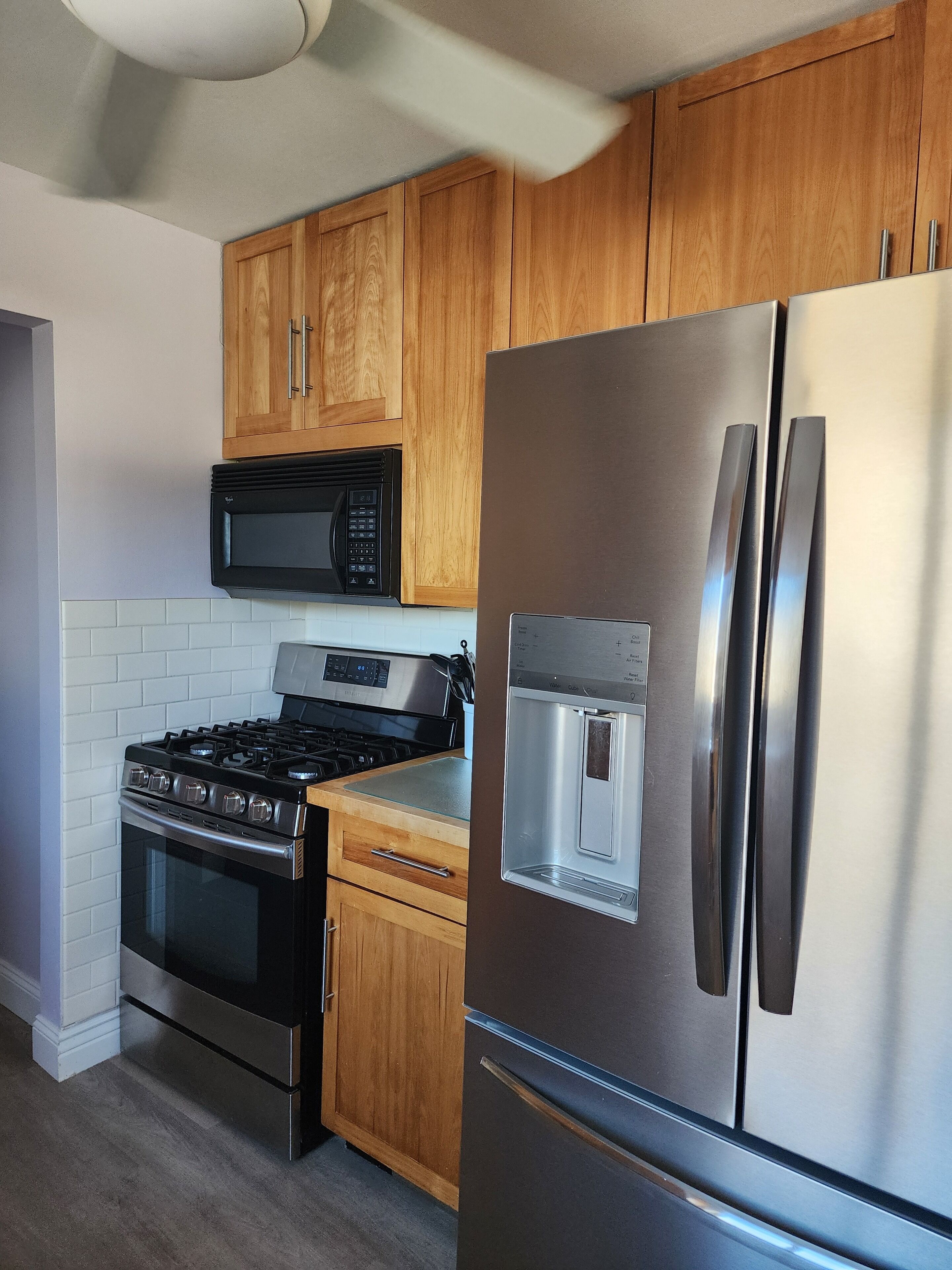 A kitchen with wooden cabinets, a stainless steel refrigerator, a microwave, and a gas stove.