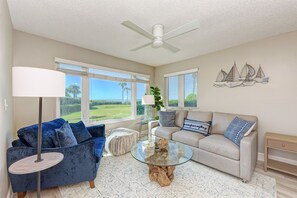 A living room with a blue sofa, a beige sofa, a glass coffee table, a floor lamp, and a ceiling fan. - GULF FRONT CONDO / PRIVATE PATIO / STEPS TO THE BEACH (Longboat Key)