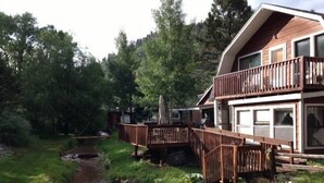 A two-story wooden cabin with a deck and a small stream in the yard.