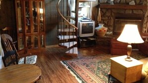 A cozy room with a spiral staircase, a fireplace, a television, and a wooden cabinet.
