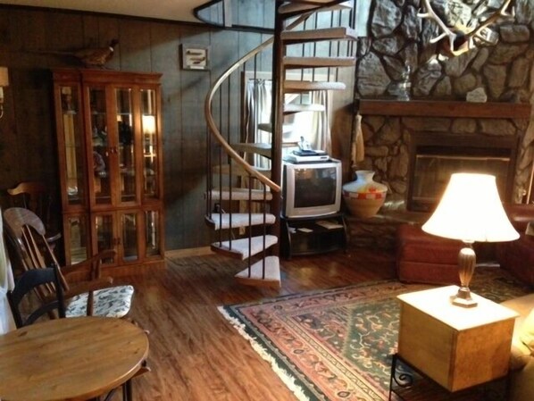 A cozy room with a spiral staircase, a fireplace, a television, and a wooden cabinet. - Stream-side Mountain Home (Cascade-Chipita Park)