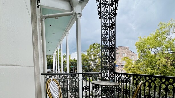 A covered balcony with two chairs and a table, white walls, and a view of trees and buildings.