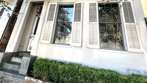 A building with a balcony, large windows with shutters, and a brick-paved entrance.