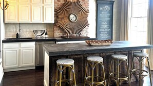 A kitchen with white cabinets, a brick accent wall, a large mirror, and a menu board.