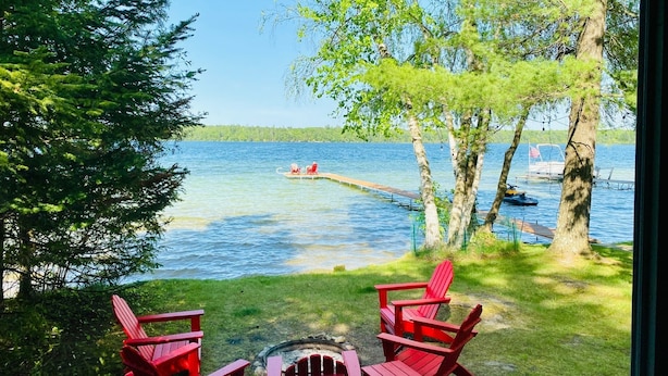 A lakeside view with red Adirondack chairs, a dock, and boats. - Green Lake: Charming Cottage with Sandy Beach & Dock - Ideal for Family Getaways (Interlochen)