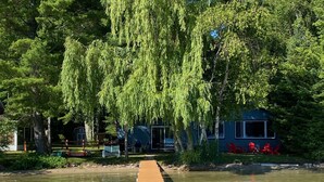 A lakeside cabin with a dock extending into the water, surrounded by trees. - Green Lake: Charming Cottage with Sandy Beach & Dock - Ideal for Family Getaways (Interlochen)