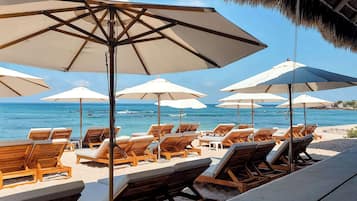Un área de descanso frente a la playa, con sillones de madera y sombrillas grandes, con vista al océano.