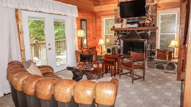L’intérieur d’un chalet confortable, avec des murs en rondins de bois, une cheminée en pierre, des fauteuils en cuir et un téléviseur fixé au-dessus de la cheminée.