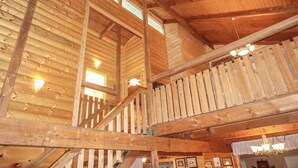 Un intérieur en bois avec un escalier, des poutres apparentes et un lustre.