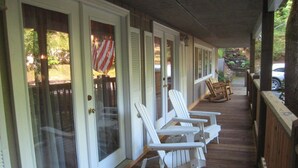 Une véranda couverte avec des fauteuils Adirondack blancs, une terrasse en bois et, au loin, on aperçoit un véhicule.