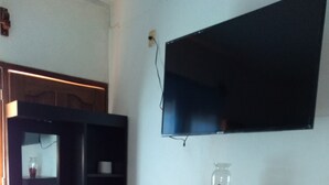 A room with a dark wooden cabinet with drawers, a flat-screen TV mounted on the wall, and a small vase with red flowers on top of the cabinet. - Pacefull Condo in Puerto Vallarta  (Lomas del Coapinole)