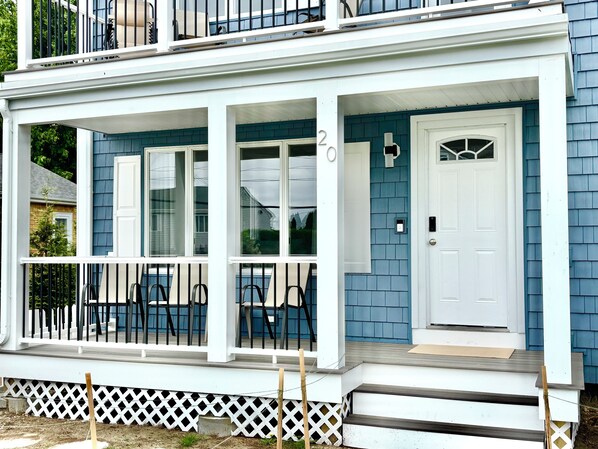 A two-story house with a covered porch, white railings, and a white door.
